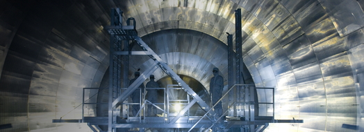 Blick ins Innere von KATRIN, dem Neutrino-Experiment am KIT: Man sieht die Innenwand einer riesigen Stahlröhre. Auf einem Gerüst sind drei Personen in Schutzanzügen zu sehen. (Foto: Markus Breig, KIT)